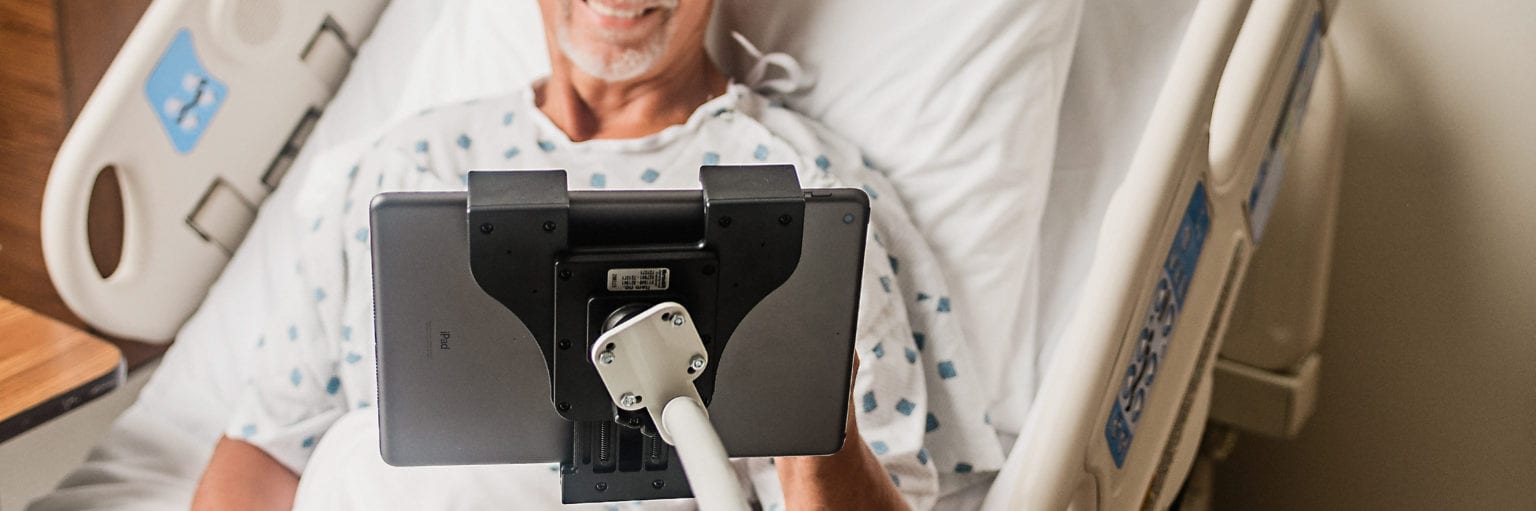 Man in hospital bed using a device on a flex arm