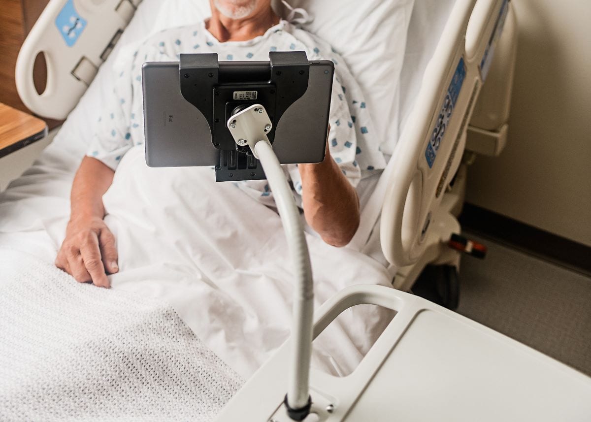 Man in hospital bed using a device on a flex arm